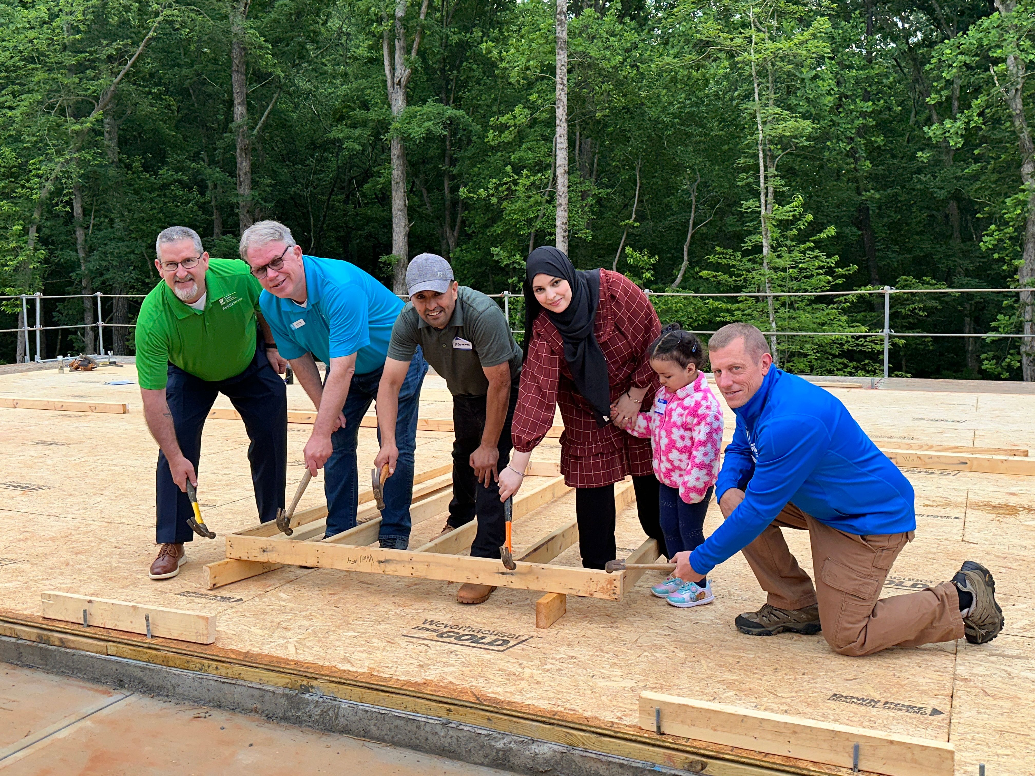 Habitat for Humanity volunteers and family hammering first nail together
